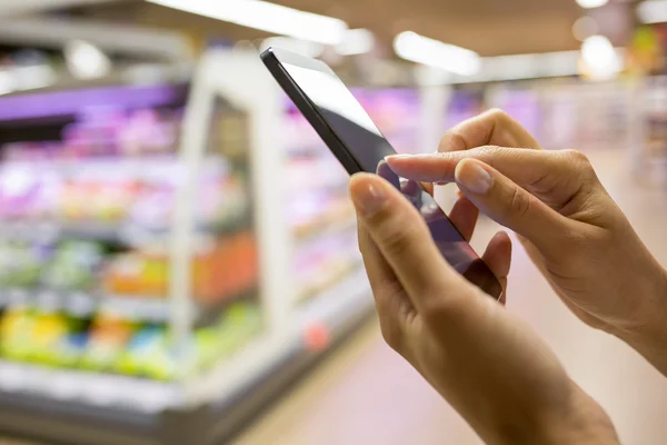 Woman using mobile phone while shopping in supermarket — Stock Photo, Image