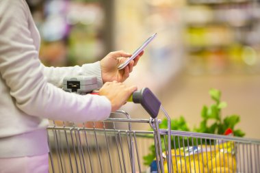 Kadın süpermarkette alışveriş yaparken cep telefonu kullanıyor