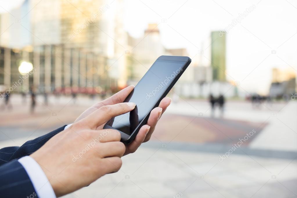 Businesswoman sending messages with her mobile phone in front of building