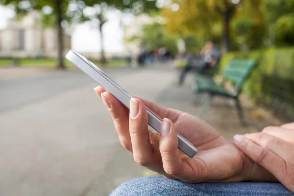 Vrouw siiting op een bank in een park met behulp van haar mobiele telefoon — Stockfoto