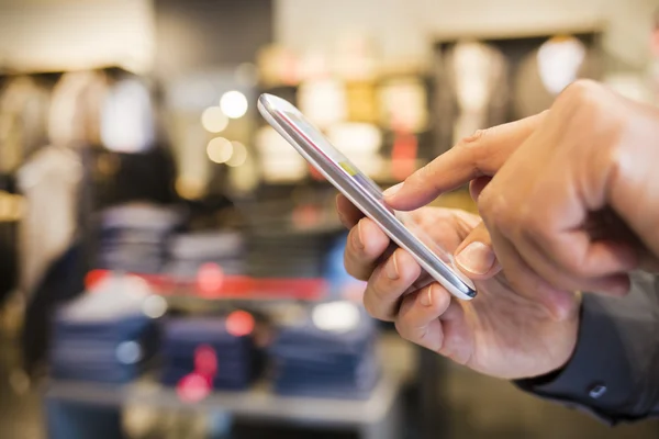 Primer plano de un hombre usando el teléfono móvil en la tienda de ropa —  Fotos de Stock