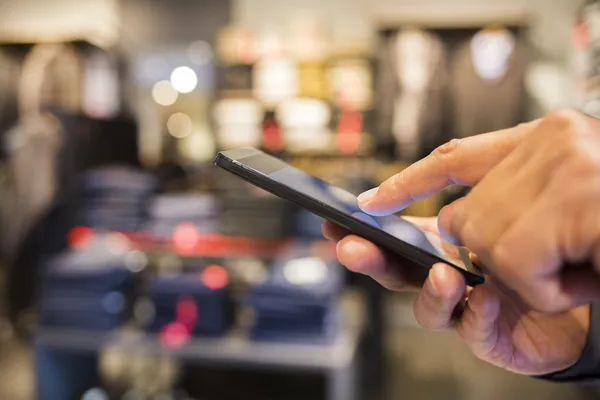 Primer plano de un hombre usando el teléfono móvil en la tienda de ropa — Foto de Stock