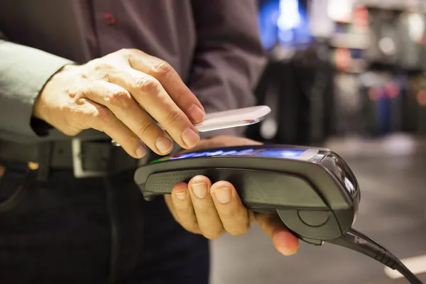 Hombre que paga con tecnología NFC en el teléfono móvil, en la tienda de ropa — Foto de Stock