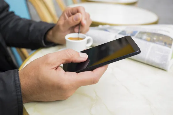 Homem usando um telefone celular no terraço do café, papel de notícia e café — Fotografia de Stock