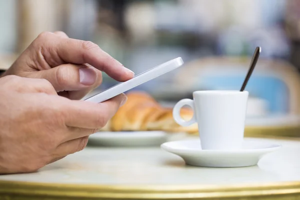 Hombre usando un teléfono celular en la terraza de la cafetería, croissant y café —  Fotos de Stock