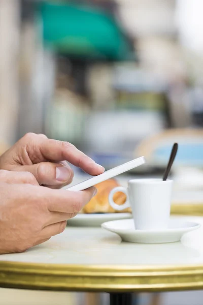 Człowiek za pomocą telefonu komórkowego na tarasie kawiarni, rogalik i kawa — Zdjęcie stockowe