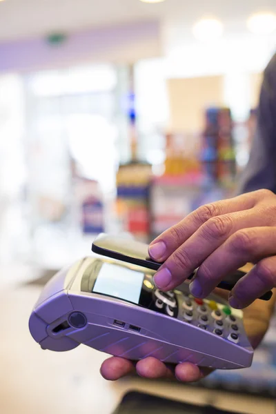 Hombre que paga con tecnología NFC en el teléfono móvil, en la farmacia — Foto de Stock