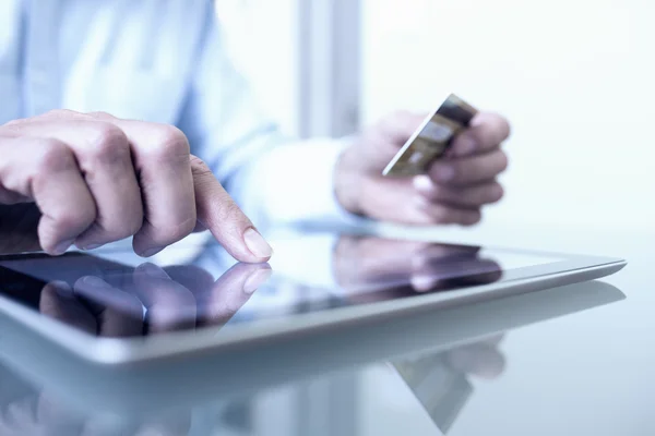 Elinde tablet ve kredi kartı olan adam içeride internetten alışveriş yapıyor.
