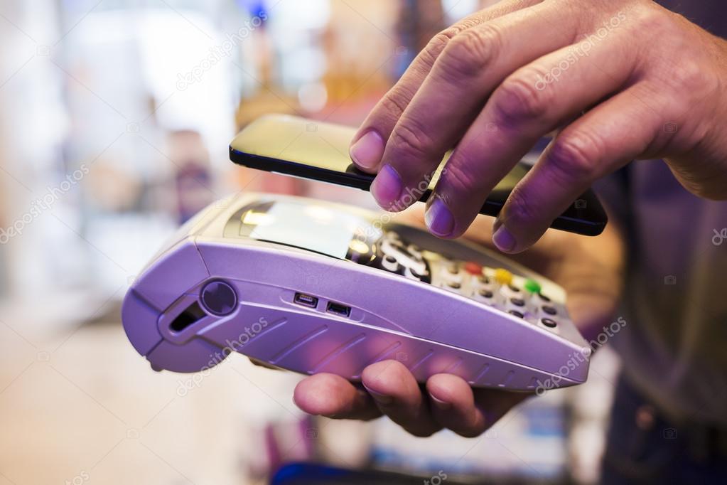 Man paying with NFC technology on mobile phone, in pharmacy