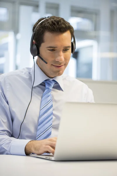 Biznesmen z zestawem słuchawkowym działa na laptopie — Zdjęcie stockowe