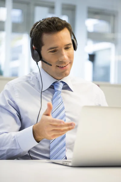 Empresário com fone de ouvido trabalhando no laptop — Fotografia de Stock