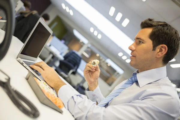 Businessman with laptop eating sushi — Stock Photo, Image