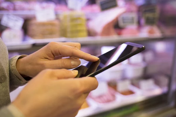 Mulher usando telefone celular enquanto faz compras no açougueiro do supermercado — Fotografia de Stock