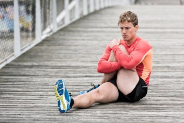 Genç atletik adam ahşap köprüde geriniyor.