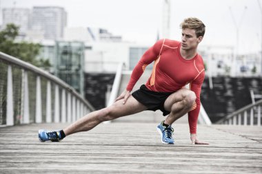 Genç atletik adam ahşap köprüde geriniyor.