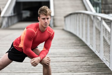 Atletik genç erkek dışarıda bacak esnetiyor.