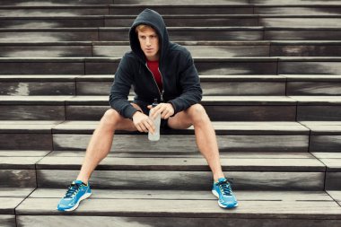 Şehir sporcusu antrenmandan sonra dinleniyor, merdivenlerde oturuyor. İçme suyu