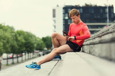 Jogger checking sport performance on his mobile phone and smartwatch app. Urban background