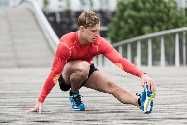 Genç atletik adam ahşap köprüde geriniyor.