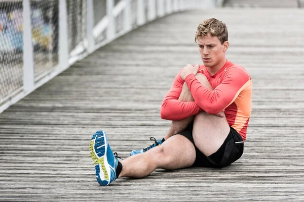 Genç atletik adam ahşap köprüde geriniyor.