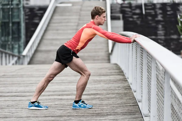 Atletik genç erkek dışarıda bacak esnetiyor.