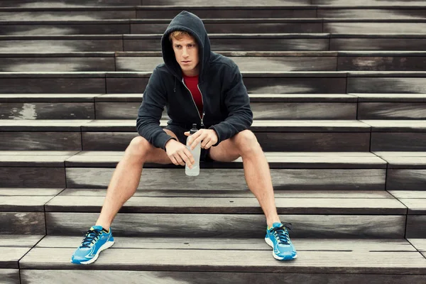 Şehir sporcusu antrenmandan sonra dinleniyor, merdivenlerde oturuyor. İçme suyu