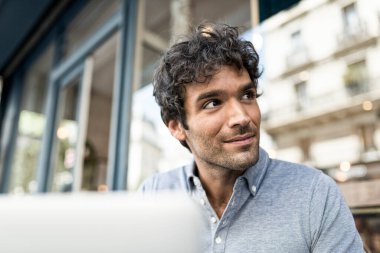 Kafe terasında dizüstü bilgisayarda çalışan genç bir adamın portresi. Şehirde bilgisayar kullanan bir iş adamı.