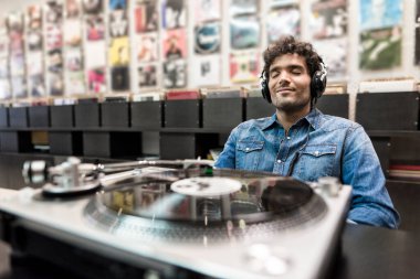 Genç adamın gözleri kapalı plak dükkanında plak dinliyor.