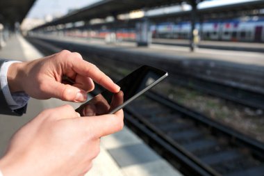Man using a mobile phone on empty railway platform. Close-up hands