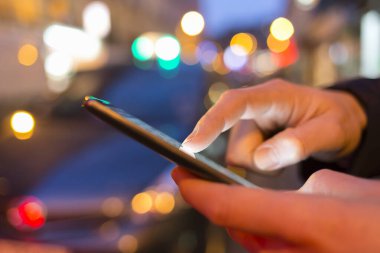 Man using his Mobile Phone in the street, night light bokeh Background clipart