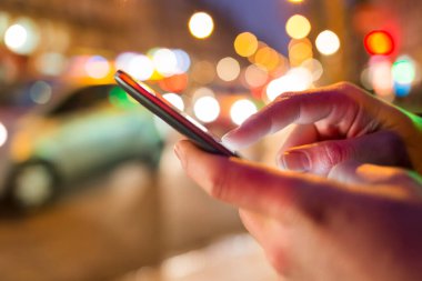 Sokakta cep telefonunu kullanan bir adam, gece lambası arka planda.