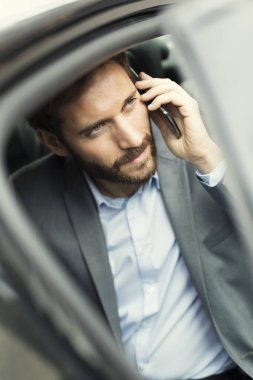 Sıradan bir iş adamı arabanın arkasında cep telefonuyla konuşuyor.