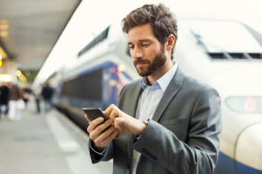 Man on platform station. Typing text message on mobile phone
