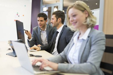 Modern bir ofiste bilgisayar üzerinde çalışan bir grup iş adamı.