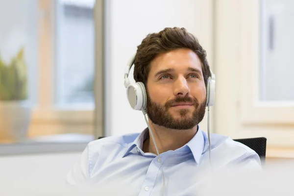 ビジネスマンはヘッドフォンで音楽を聴いている 近代事務所 — ストック写真