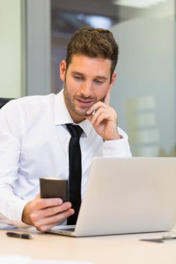 İş adamı ofisteki cep telefonundan mesaj yazıyor.