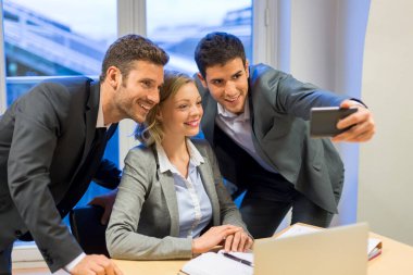 Üç iş adamı ofiste selfie çekiyor.