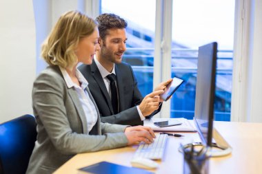 Ofiste bilgisayar ve tablet üzerinde çalışan iki iş adamı. 