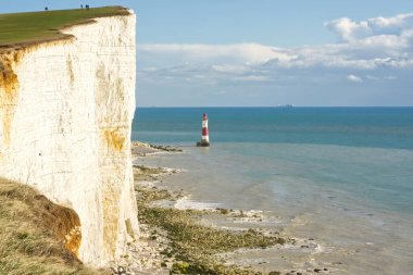 Doğu Sussex, İngiltere 'de Eastbourne yakınlarındaki Beachy Head' de tebeşir uçurumları. Uçurumun kenarında tanınmayan insanlar var. Deniz feneri ve denizde gemiler.