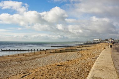Batı Sussex, İngiltere 'deki Bognor Regis' te sahil gezintisi ve tağ plajı. Arka planda iskele var. Uzakta tanınmayan insanlar.