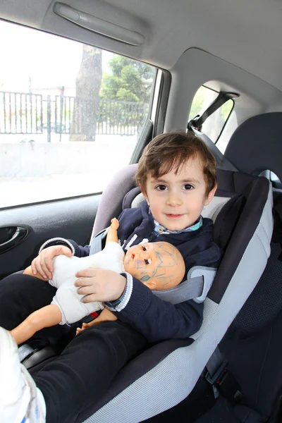 Niño con su muñeca en el asiento del coche para mayor seguridad —  Fotos de Stock