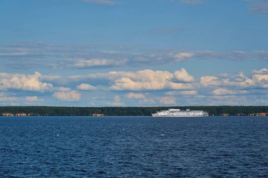 Sahilin arka planında beyaz bir gemiyle nehir manzarası ve beyaz bulutlu mavi gökyüzü.