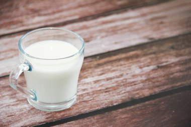 Beyaz doğal süt, şeffaf bir kupada, ahşap bir arka planda.