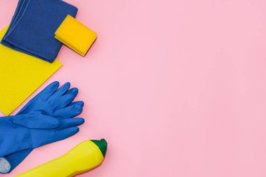 household cleaning supplies, yellow and blue rag, foam sponge, rubber gloves and cleaning cream in a yellow bottle, on a pink background