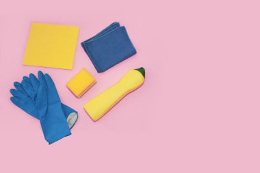 household supplies for cleaning the apartment, blue gloves, yellow foam sponge, cleaning cream in a bottle, on a pink background, top view