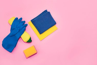 household supplies for cleaning the apartment, a blue rag, gloves and a yellow sponge on a pink background