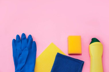 household supplies for cleaning the apartment, a blue rag, gloves and a yellow sponge on a pink background