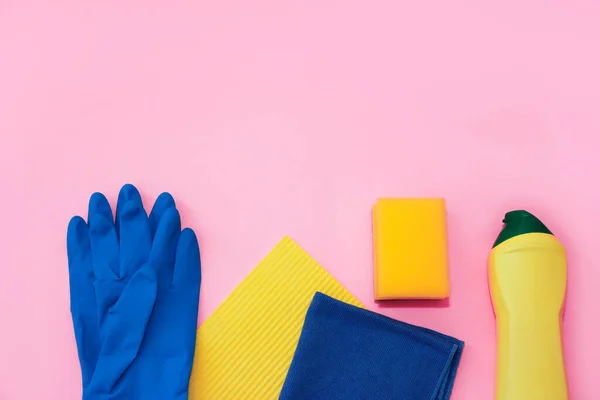 household supplies for cleaning the apartment, a blue rag, gloves and a yellow sponge on a pink background