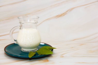 Beyaz mayalanmış süt içeceği ayran şeffaf cam bardakta mavi tabakta ve mermer gri arka planda