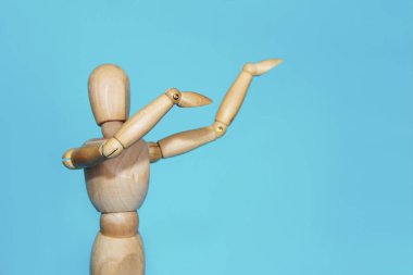 Sarı ahşap manken, elleri mavi arka planda poz ve jestler yapıyor.